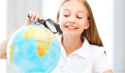 young lady smiling while looking at a globe with a magnifying glass