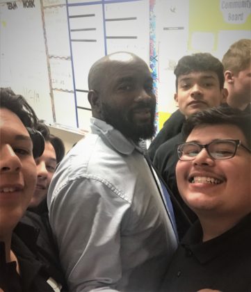 Black male math teacher surrounded by his students
