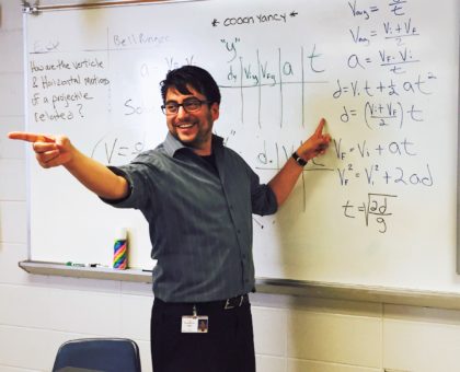 physics teacher at his white board pointing to a student who has a question